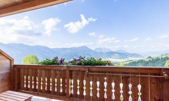 A beautiful balcony with colorful flowers and a view of the mountains. The sky is clear and the landscape is green and inviting.