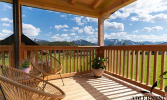 A beautiful wooden terrace with a view of mountains and a clear sky. The space is cozy, equipped with plants and a chair.
