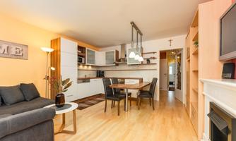 A modern kitchen with an open living area. The space is bright and welcoming, furnished with a sofa, a dining table, and modern appliances.