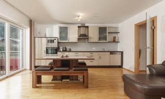 A modern kitchen with a dining area and wooden flooring. It is bright and inviting, with large windows that let in plenty of light.