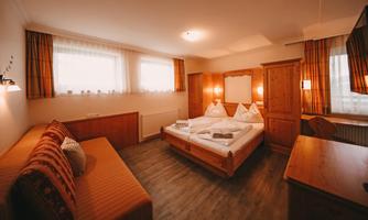 A cozy room with a double bed and a sofa bed. Bright windows and warm wooden interiors create an inviting atmosphere.