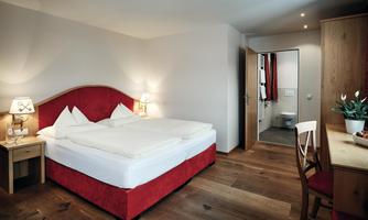 A cozy bedroom with a large double bed and wooden floor. There is a table, chairs, and access to a bathroom.