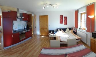 A modern living and bedroom with a red kitchen and a light wood floor. The room is warmly lit and well-furnished, making it ideal for a relaxed atmosphere.