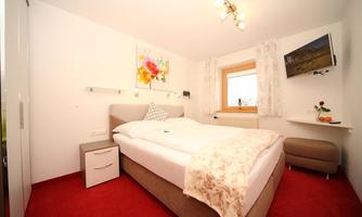 A cozy bedroom with a large bed and red carpet. There is a television and decorative elements on the walls.