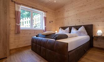 A cozy bedroom with wooden walls and a large bed. Next to the bed are nightstands, and the windows let in plenty of daylight.