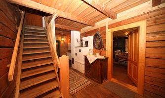 A cozy entrance area with a wooden staircase and rustic walls. To the right is an open door leading to another room.