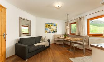 A modern living and dining room with a gray sofa and a dining table. Large windows provide plenty of daylight and a pleasant atmosphere.