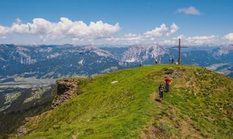 A beautiful mountain peak with an observation platform and a large cross. In the background, majestic mountains and a clear sky can be seen.
