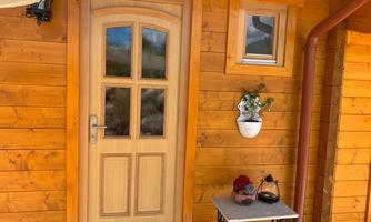 A wooden door with a window frame, surrounded by a wooden wall. Next to the door is a small table with a lantern and a floral decoration.