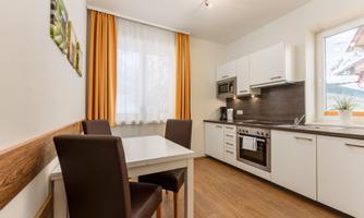 A modern kitchen with elegant furniture and a table for four people. The large windows let in plenty of light and offer a lovely view outside.