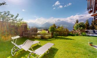 A beautiful garden with loungers and a view of the mountains. The sky is clear and the surroundings are green and inviting.