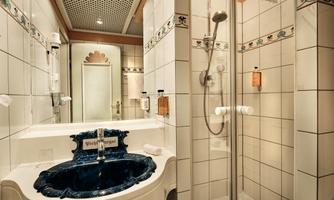 An elegant bathroom with a blue wash basin and a separate shower. The walls are adorned with white tiles and decorative elements.