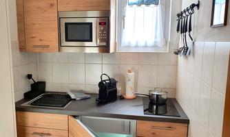 A modern kitchen with wooden cabinets and a microwave oven. It also includes a coffee machine and various kitchen utensils.