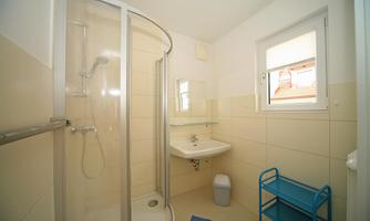 A modern bathroom with a shower and a sink. There is a window and a blue towel rack.