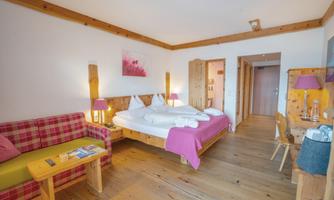A cozy hotel room with a double bed and a living area. Wooden decor and an inviting atmosphere make the space friendly and warm.