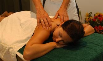 A woman is receiving a back massage on a treatment table. The room is relaxing, decorated with a towel and flowers.