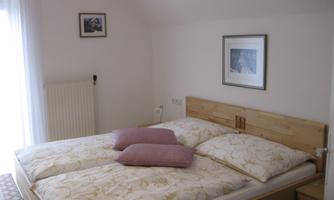 A cozy bedroom with a double bed and two pillows. The walls are bright, and there is a window with curtains as well as some pictures.