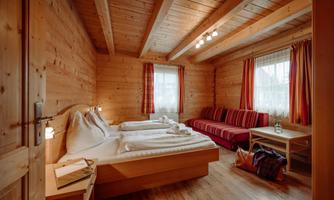 A cozy bedroom made of wood with a double bed and a red sofa. The windows are decorated with curtains, and the room has a warm, inviting atmosphere.