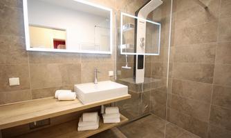 A modern bathroom with a shower and an elegant sink. The walls are clad with neutral tiles, and there is a lit mirror.