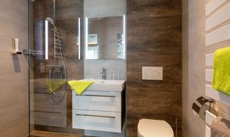 A modern bathroom with a shower, a sink, and a toilet. The walls are painted in neutral tones, and a green towel adds a splash of color.