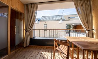 A cozy balcony with a wooden floor and a wooden table. The large windows let in plenty of light and offer a view of the surroundings.