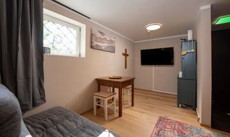 A cozy room with a table and two chairs.  
On the wall hangs a television and there is a window with a view outside.