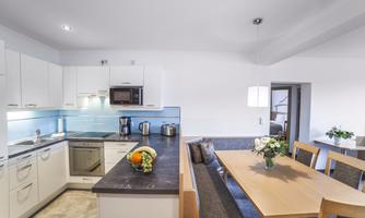A modern kitchen with white cabinets and a dining group. Fresh fruit and a bouquet of flowers are on the table.