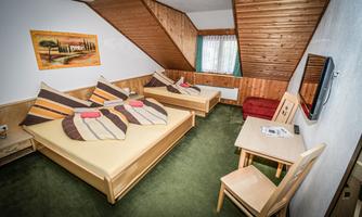 A cozy room with two beds and colorful cushions. There is a table, a chair, and a television on the wall.