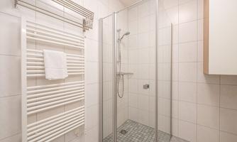 A modern bathroom with a glass shower. The walls are light tiled and a towel holder with a white towel is visible.