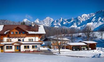 A charming house in winter snow, surrounded by majestic mountains. The clear blue sky completes the stunning landscape.