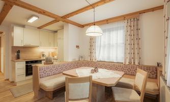 A bright kitchen with a cozy wooden dining area. The room has large windows and a warm atmosphere.