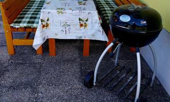 A cozy table with a checkered tablecloth and two benches is set outside. Next to the table is a round grill.