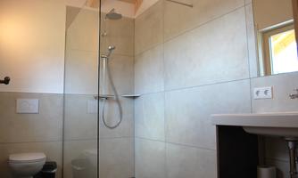 A modern bathroom with a walk-in shower and bright tiled flooring. The sink is placed next to the shower, and there is plenty of natural light.