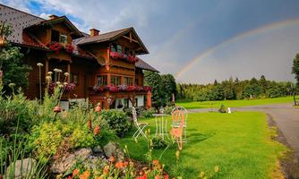 A beautiful wooden house surrounded by green grass and colorful flowers. In the background, a rainbow can be seen.