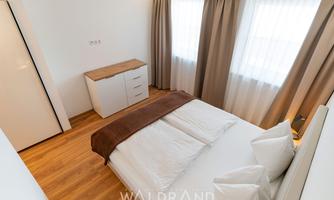 A modern bedroom with a large bed and bright curtains. The wooden floor and simple furniture create an inviting atmosphere.