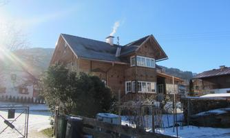 A beautiful wooden house in winter with snow and a blue sky. Smoke rises from the chimney.