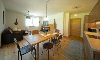 A modern kitchen with a dining area and a cozy living area. The room is bright and inviting, furnished with wooden and metal furniture.