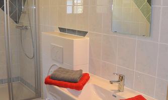 A modern bathroom with a shower and a sink. Red towels are neatly arranged.