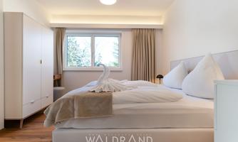 A modern bedroom with a large double bed and elegant pillows. The bright decor and the window create a friendly atmosphere.