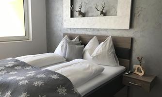A cozy bedroom with a large bed and white pillows. Ornamental antlers hang on the wall, and a modern design characterizes the room.