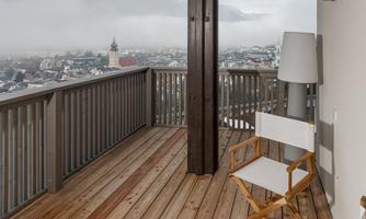 A cozy terrace with a wooden floor and two chairs. In the background, a misty landscape with a city view can be seen.