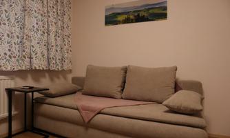 A cozy sofa with cushions in a bright room. Next to the sofa is a small table, and a picture hangs on the wall.