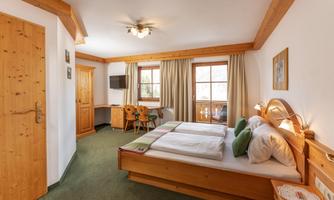 A cozy bedroom with a large bed and wooden furniture. Large windows let in plenty of light and offer a view of the surroundings.