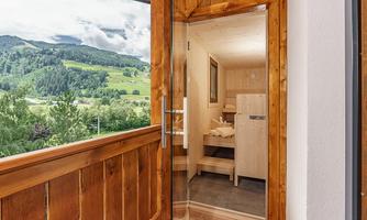 An open window with a view of green hills and a spacious wooden terrace. The interior is designed in a modern and minimalist style.