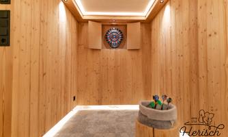 A cozy room with wood paneling and soft lighting. In the center, there is a dartboard and a container with darts.