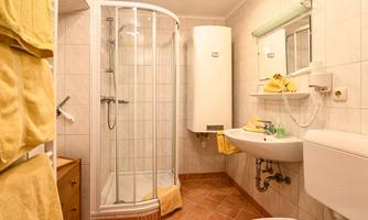 A small bathroom with a shower cabin and a sink. Yellow towels hang on the wall and there is a mirror above the sink.