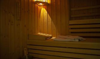 A cozy wooden sauna with warm light. On the bench lie a towel and a wooden container.