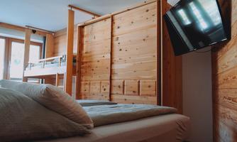 A cozy room with wooden walls and a bed. A TV is mounted on the wall, and the window lets in a lot of light.