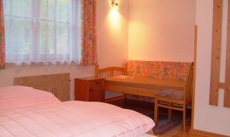 A simple room with a bed and a small seating area. The window lets in plenty of daylight.