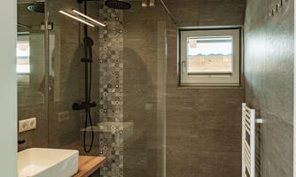 A modern bathroom with a rain shower and clean lines. The walls are in an elegant gray tone and there is a bright window.